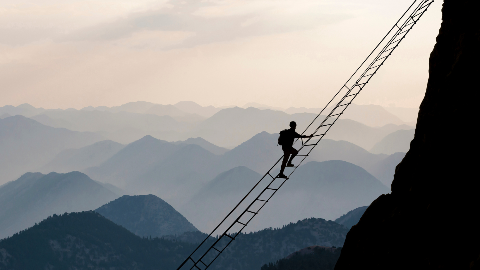 Man climbing precarious ladder while looking out over distant mountains.